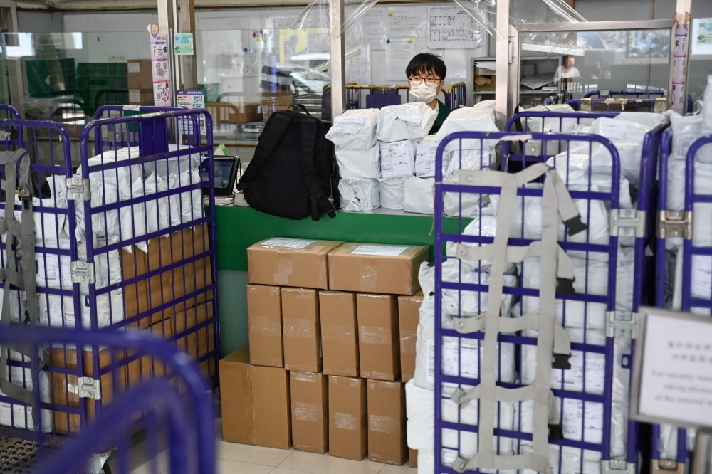 Stacked parcels are seen up front as a Hongkong Post employee stands at a service counter at a post office in Hong Kong on April 16, 2025. (Photo by Peter Parks / AFP)