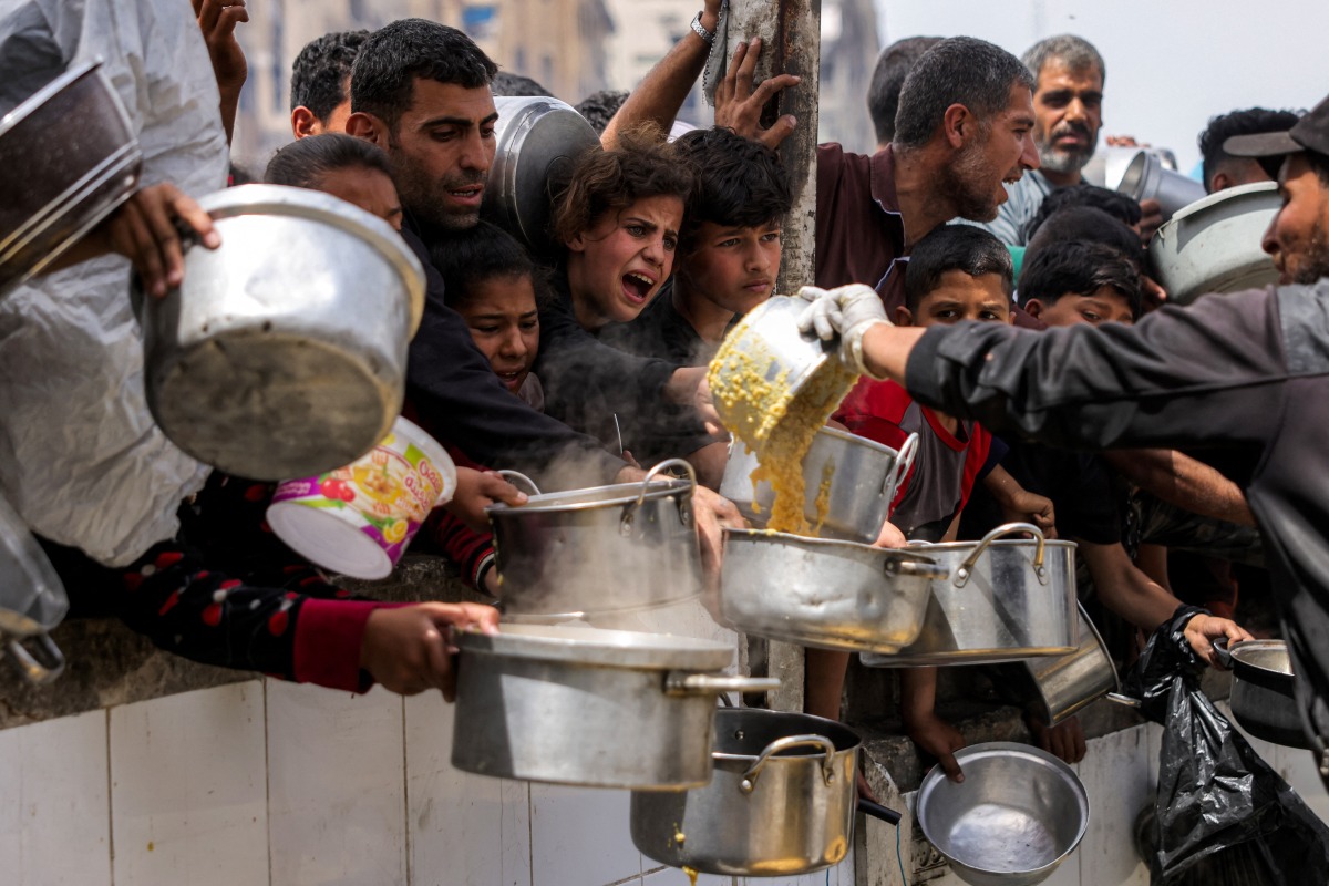 People queue with pots to receive charity meals from a kitchen in Beit Lahia in the northern Gaza Strip on April 24, 2025. Israel on March 18 resumed its intense military offensive in the Palestinian territory after a ceasefire deal that came into effect on January 19 fell apart two months later over differences regarding its next phase. (Photo by Bashar TALEB / AFP)