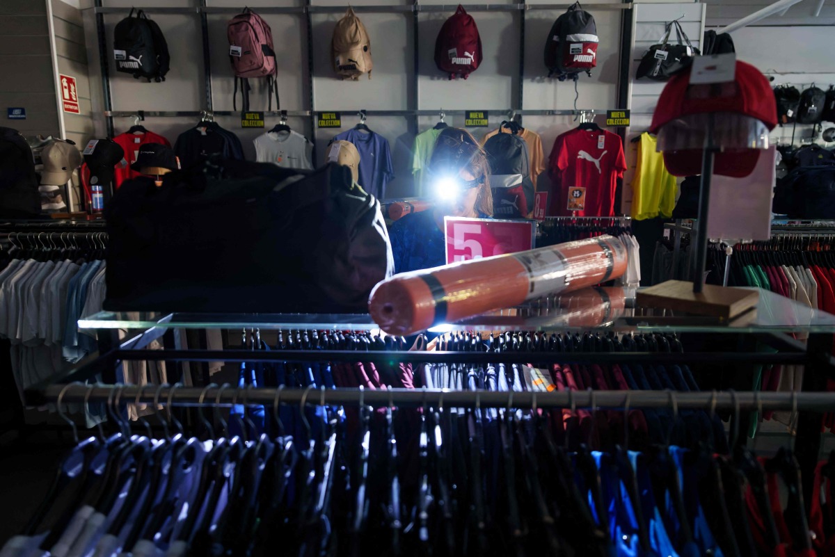 A saleswoman at a sports store works with a light on her head in Burgos on April 28, 2025, during a massive power cut affecting the entire Iberian peninsula and the south of France. (Photo by CESAR MANSO / AFP)
