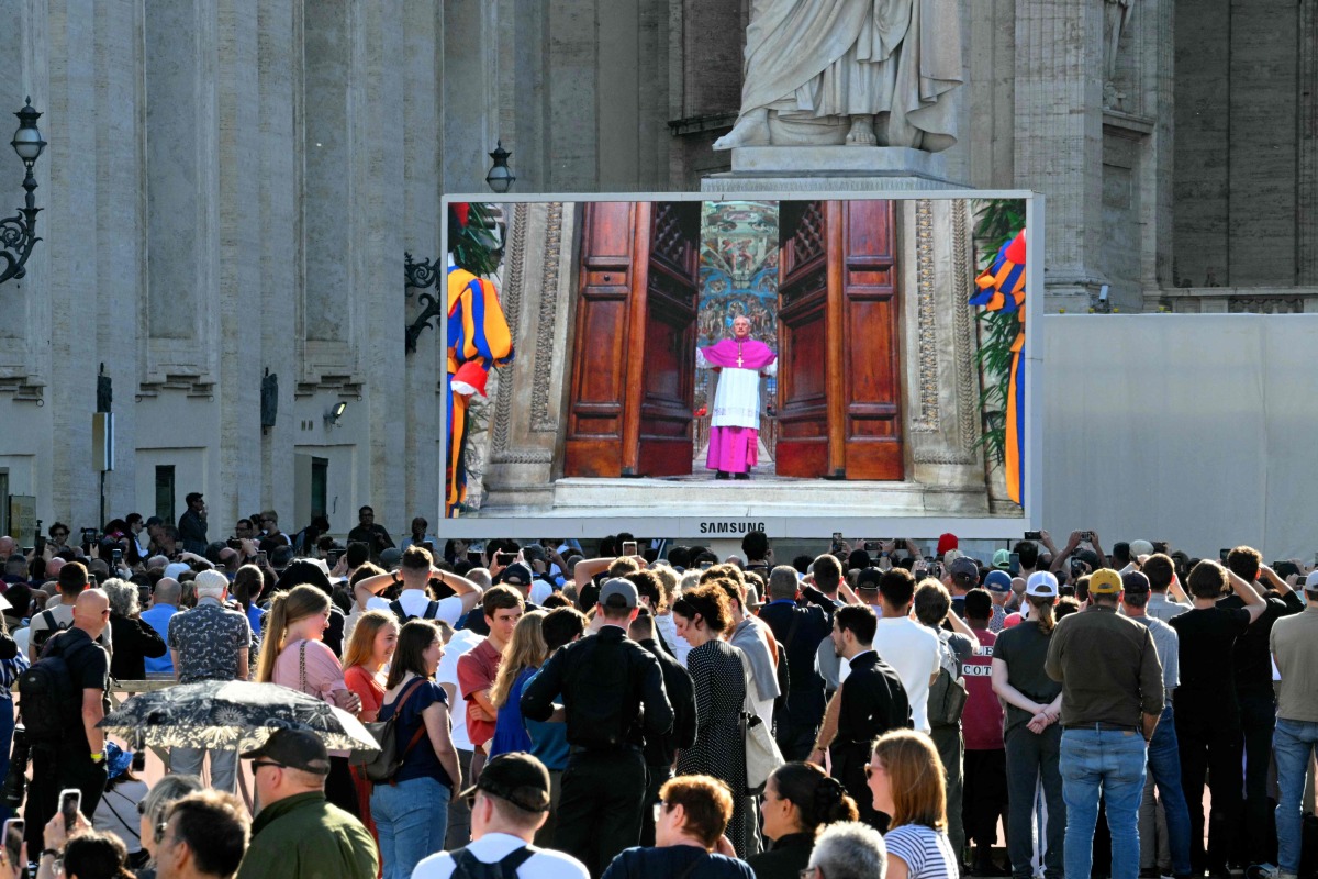 Faithful watch a giant screen displaying images of Diego Giovanni Ravelli, Master of Pontifical Liturgical Celebrations, closing the doors of the Sistine chapel as the conclave to elect a new Pope starts, at St Peter's Square in The Vatican, on May 7, 2025. (Photo by Andreas SOLARO / AFP)