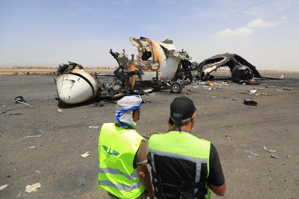 Airport employees stand next to a destroyed plane at the Sanaa International Airport on May 7, 2025. (Photo by Mohammed Huwais / AFP)