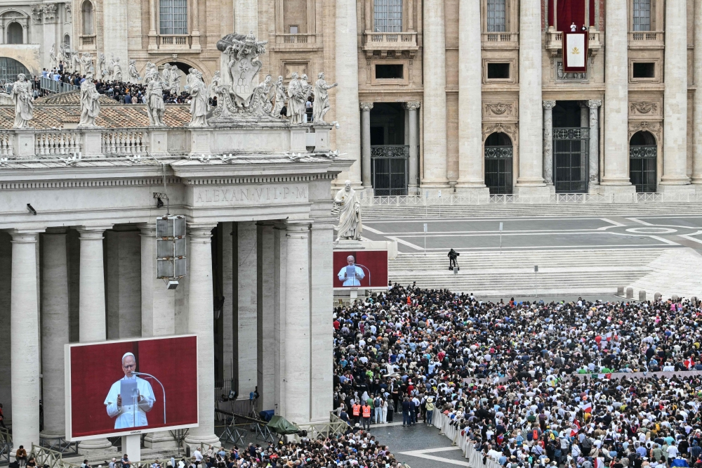 Faithfuls gather as Pope Leo XIV is seen on giant screens as he delivers the Regina Caeli prayer from the main central loggia of St Peter's basilica in The Vatican, on May 11, 2025. (Photo by Stefano Rellandini / AFP)
