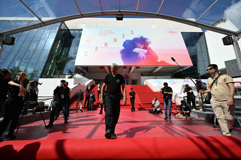 An employee (C) unrolls the red carpet at the Palais des Festivals ahead of the opening ceremony 78th Cannes Film Festival in Cannes, south-eastern France, on May 13, 2025. (Photo by Bertrand Guay / AFP)