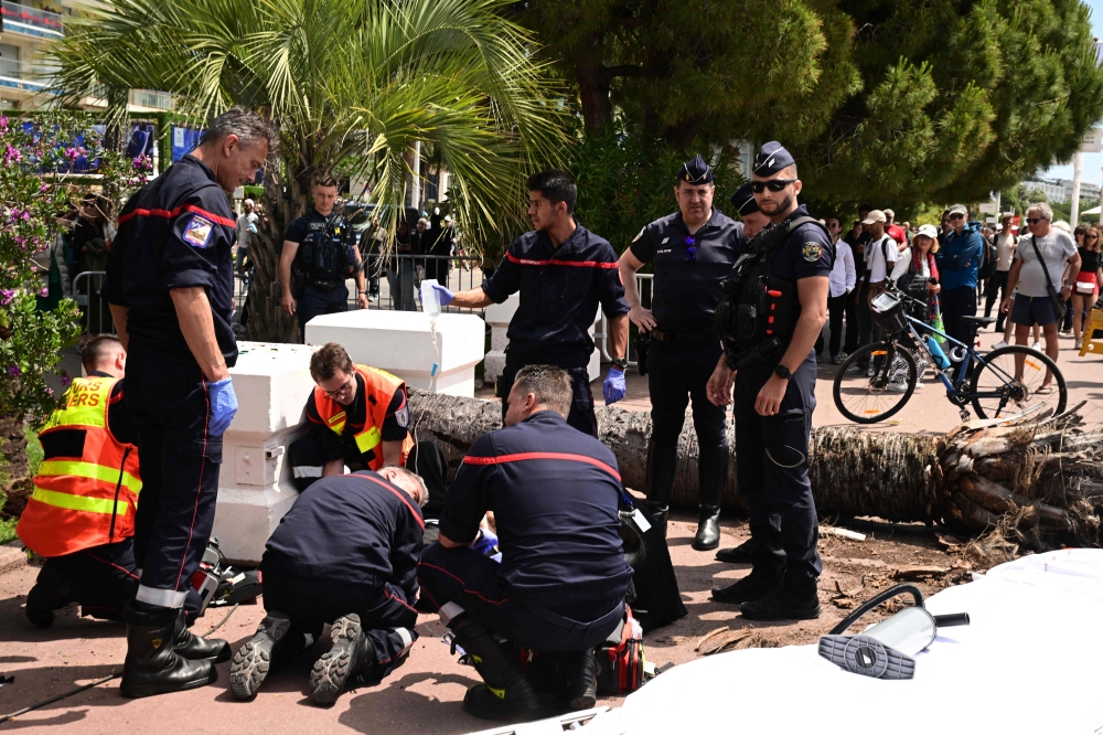 Emergency services assist a passerby injured after an old palm tree fell along the Boulevard de la Croisette, on May 17, 2025. (Photo by Miguel Medina / AFP)
 