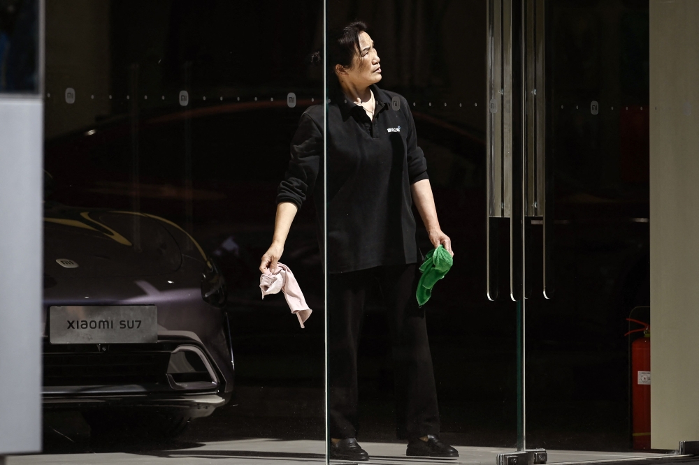 A cleaner looks on at a Xiaomi store in Beijing on May 19, 2025. (Photo by Wang Zhao / AFP)