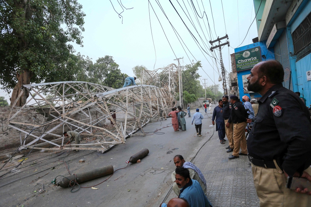 Pakistani policemen look on as workers remove a fallen railway tower after a storm in Multan on May 28, 2025. (Photo by Shahid Saeed Mirza / AFP)