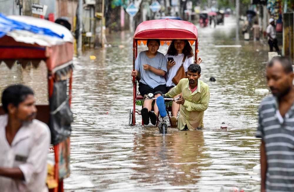 Women commute in cycle rickshaws through a flooded street after heavy rains in Guwahati, in India's Assam state on May 31, 2025. (Photo by Biju Boro / AFP)