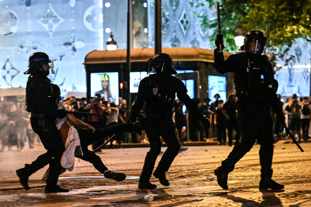 Anti-riot police officers detain a person as Paris Saint-Germain supporters celebrate after PSG won the UEFA Champions League final football match between Paris Saint-Germain (PSG) and Inter Milan held in Munich, on the Champs-Elysees avenue in Paris on May 31, 2025. (Photo by Lou Benoist / AFP)