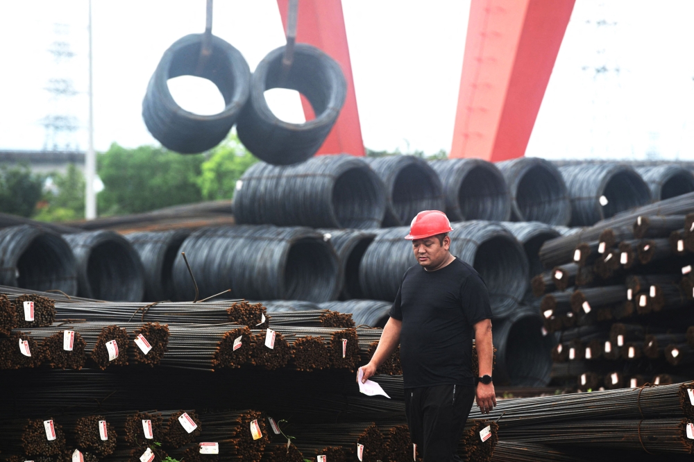 A worker walks past rolls of steel at a steel market in Hangzhou, in eastern China's Zhejiang province on June 4, 2025. (Photo by AFP) 