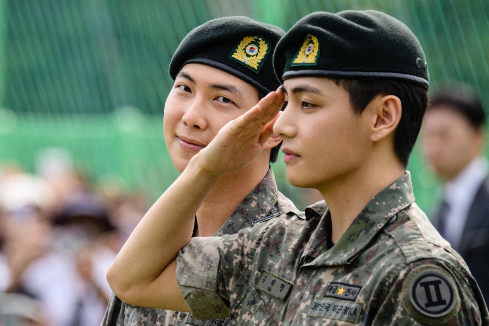 K-pop boy band BTS member V (R) salutes as RM looks on at an outdoor sporting facility in Chuncheon on June 10, 2025. (Photo by Anthony Wallace / AFP)