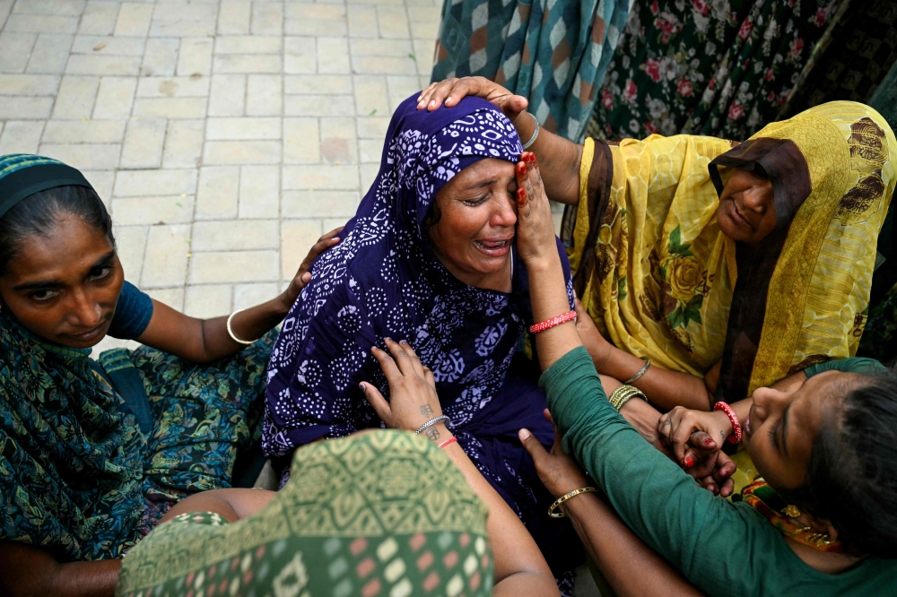 Women mourn their relatives killed the previous day after Air India flight 171 crashed in a residential area, whilst waiting outside hospital mortuary in Ahmedabad on June 13, 2025. (Photo by Punit PARANJPE / AFP)