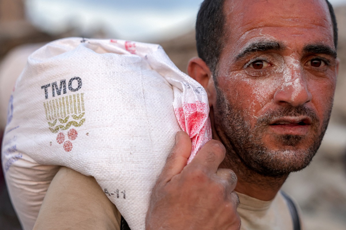 A man walks with a sack of flour on his back with others along al-Rashid street in western Jabalia on June 17, 2025, after humanitarian aid trucks reportedly entered the northern Gaza Strip through the Israeli-controlled Zikim border crossing. Photo by BASHAR TALEB / AFP.