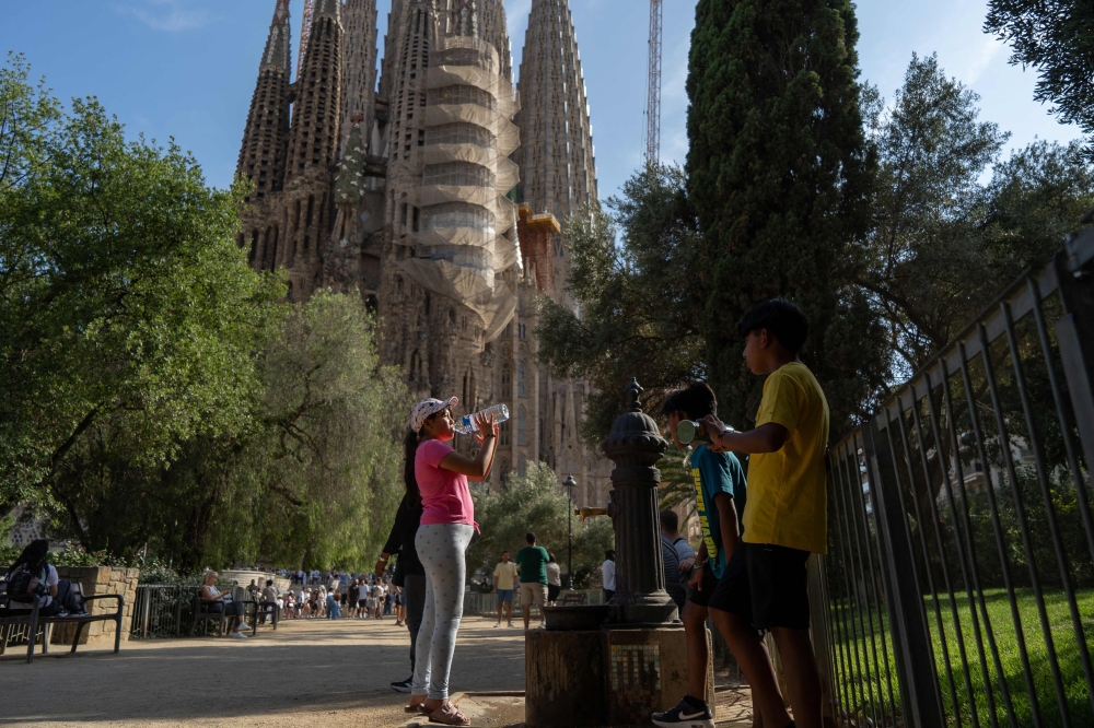People refill their bottles at a public fountain in front of the Sagrada Familia basilica in Barcelona, on June 27, 2025, a day before the first heatwave of the year is officially expected to begin. (Photo by Manaure Quintero / AFP)