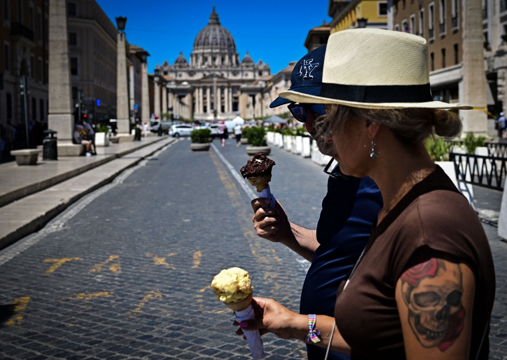 People walk while eating ice cream on a hot summer day in Rome near the Vatican on June 28, 2025. (Photo by Tiziana Fabi / AFP)