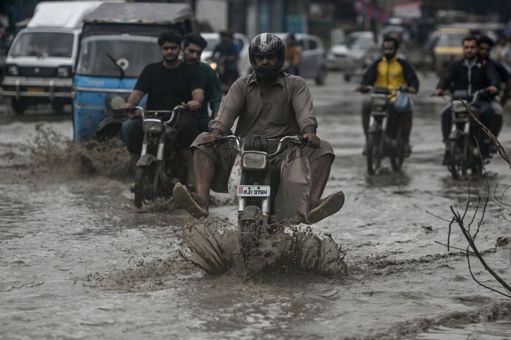 Commuters make their way through a flooded street after heavy rainfall in Karachi on June 28, 2025. (Photo by Rizwan Tabassum / AFP)

