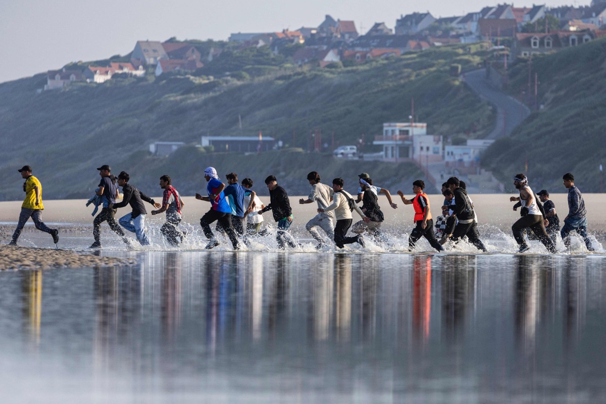 Migrants rush to try to board a smuggler's boat in an attempt to cross the English Channel on the beach of Equihen, northern France, on June 30, 2025. (Photo by Sameer Al-DOUMY / AFP)
