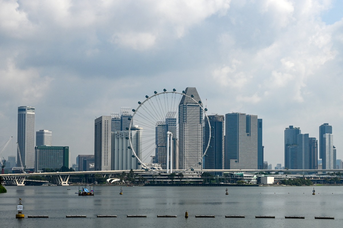 This photo shows the Singapore Flyer observation wheel (C) backdropped with the city skyline in Singapore on June 27, 2025. (Photo by Roslan RAHMAN / AFP)
