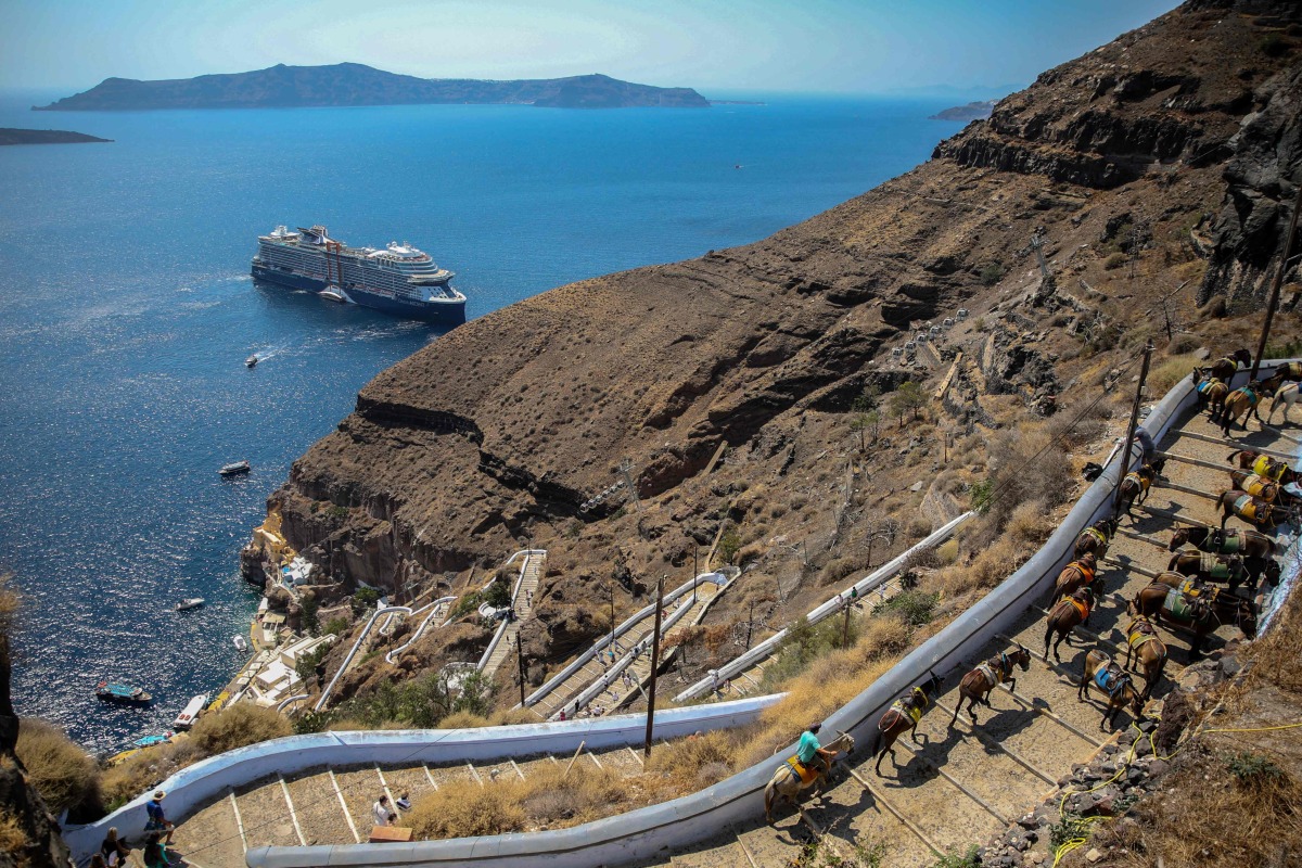 This file photograph shows a cruise ship arriving at the Greek island of Santorini while tourists on mules head to the village of Fira on July 19, 2024. Photo by ARIS OIKONOMOU / AFP