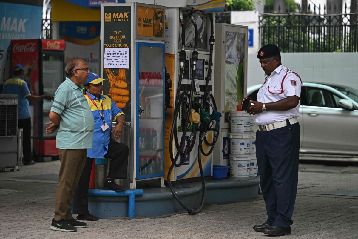 A traffic police personnel and a fuel attendant stand near a notice announcing the ban on refuelling petrol cars older than 15 years and diesel vehicles older than 10 years, displayed at a gas station in New Delhi on July 1, 2025. Photo by Arun SANKAR / AFP