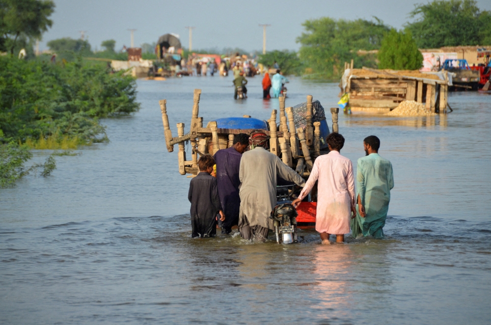 File photo for representational purposes only. Men walk along a flooded road with their belongings, following rains and floods during the monsoon season in Sohbatpur, Pakistan, August 28, 2022. (REUTERS/Amer Hussain)