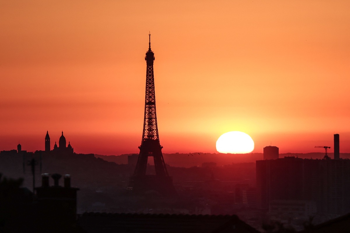 The sun rises by the Eiffel Tower and the Sacre Coeur Basilica ontop of the Montmartre hill in Paris on July 1, 2025, as the city is on red alert for high temperatures, with the top of the Eiffel Tower shut, polluting traffic banned and speed restrictions in place as a searing heatwave gripped Europe. Photo by Thibaud MORITZ / AFP