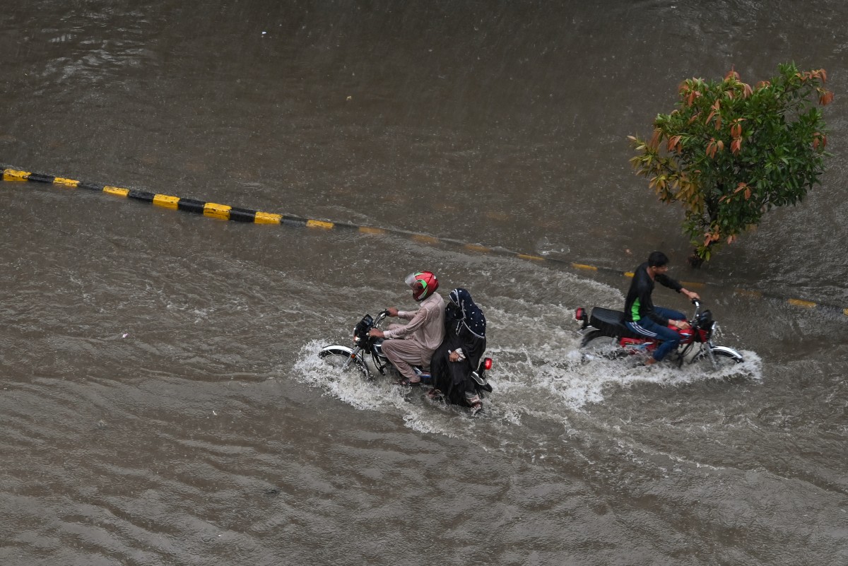Commuters wade through a flooded street following heavy monsoon rains in Lahore on July 10, 2025. (Photo by Arif ALI / AFP)
