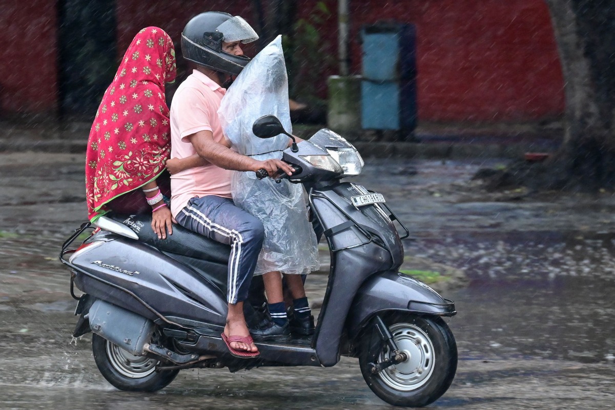 A schoolboy covered in a plastic sheet clings to an elder driving a scooter amid rainfall in India on July 16, 2025. (Photo by AFP)
