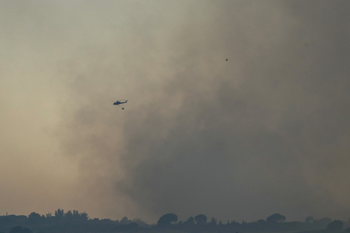 A firefighting helicopter flies through smoke from a wildfire which started in the municipality of Mentrida near Toledo, as seen from Arroyomolinos, outside Madrid on July 17, 2025. Photo by JAVIER SORIANO / AFP.

