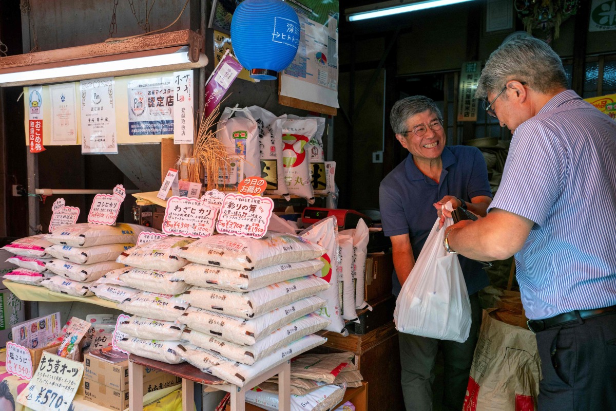 A rice mill shopowner (2nd R) tends to a customer in Tokyo on July 18, 2025. Photo by Kazuhiro NOGI / AFP