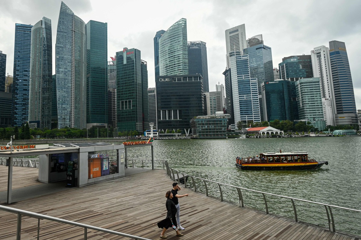 People walk as a cruise boat moves along the water at Marina Bay in Singapore on January 27, 2025. (Photo by Roslan RAHMAN and ROSLAN RAHMAN / AFP)

