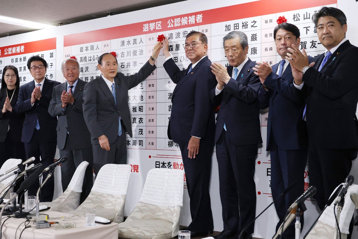 Japan's Prime Minister Shigeru Ishiba (centre R) and LDP vice president Yoshihide Suga (4th L) place a flower on the name of a candidate who is certain to win with other party members, at the vote counting centre at Liberal Democratic Party (LDP) headquarters in Tokyo on July 20, 2025.  (Photo by JIJI Press / AFP)