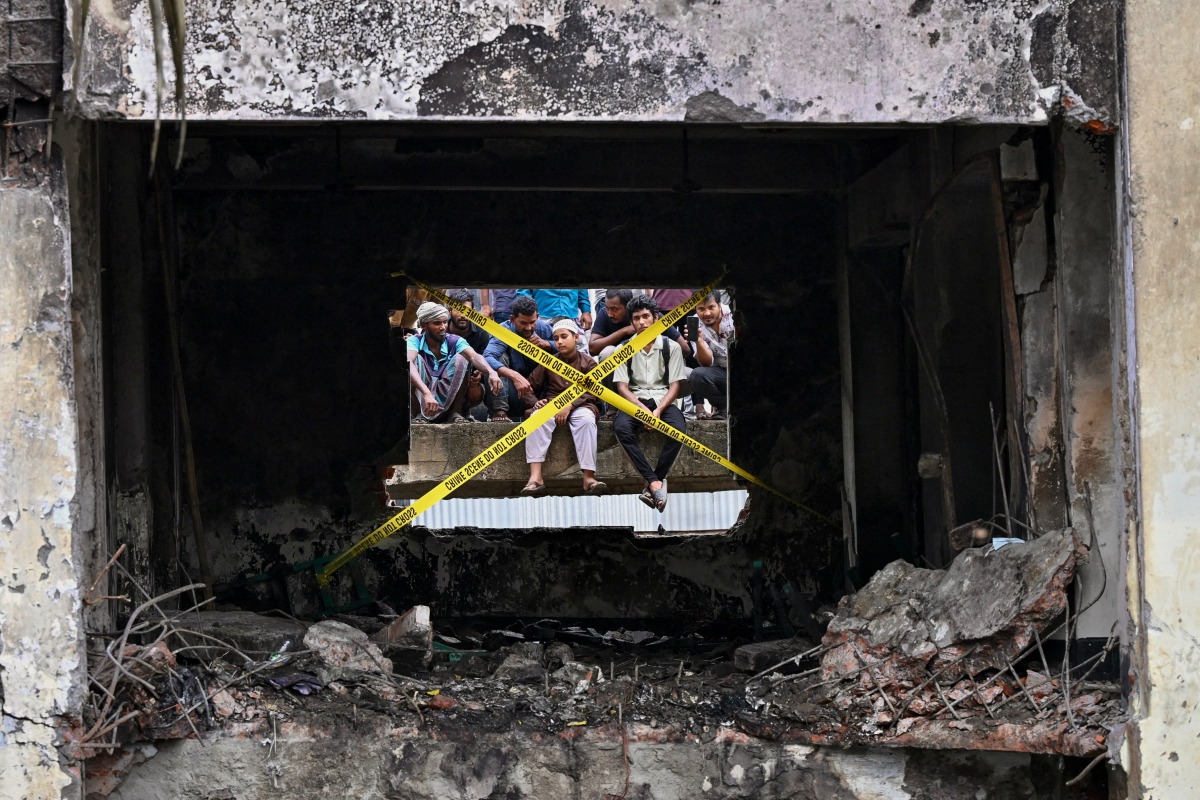 Onlookers gathered behind crime scene barrier tape cordoning off the area where Bangladesh Air Force personnel inspected the crash site a day after a training jet crashed into a school in Dhaka on July 22, 2025. Photo by MUNIR UZ ZAMAN / AFP
