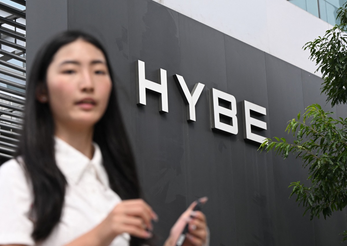 A woman walks past the signage for HYBE, the agency behind K-pop megastars BTS, displayed outside the company's headquarters in Seoul on July 24, 2025. Photo by Jung Yeon-je / AFP