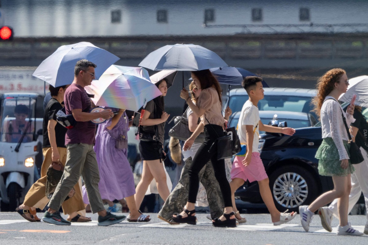 People cross a street under the hot sun in Tokyo on July 24, 2025. (Photo by Kazuhiro NOGI / AFP)
