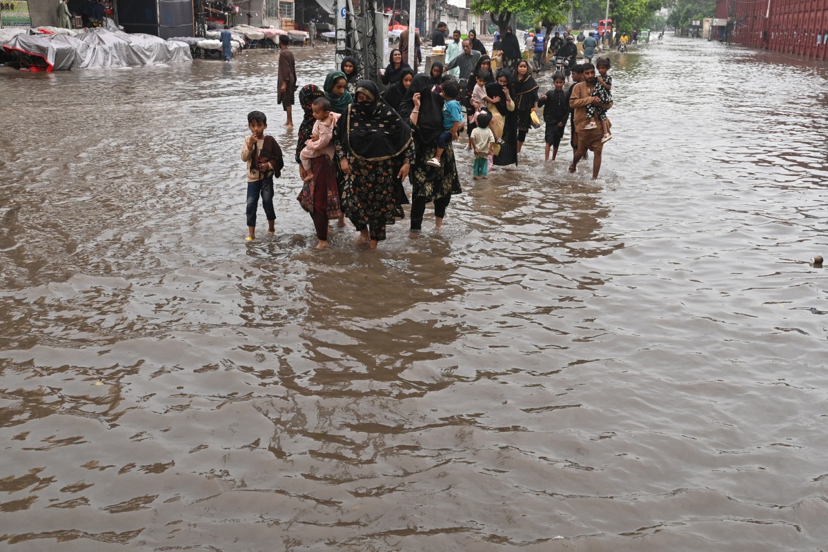 Commuters wade through a flooded street after heavy rainfall in Lahore on July 23, 2025. (Photo by Arif ALI / AFP)