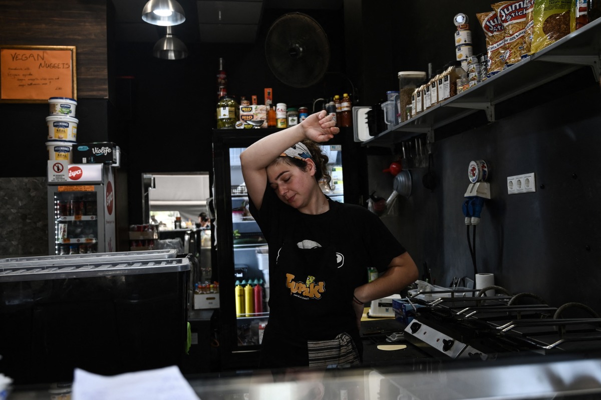 A catering employee wipes her face as she works in a small street-facing restaurant during a heatwave in Thessaloniki on July 24, 2025. (Photo by Sakis Mitrolidis / AFP)
