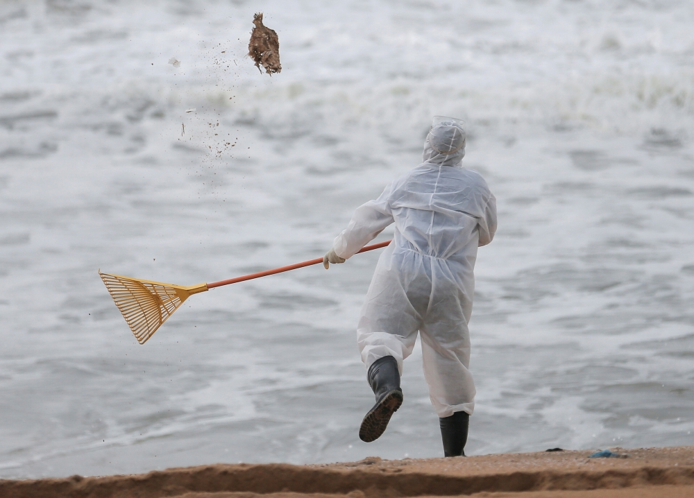 A Sri Lankan navy member throws a dead fish back to water while cleaning the debris washed to a beach from the MV X-Press Pearl container ship which caught fire and sank off the Colombo Harbour, in Ja-Ela, Sri Lanka June 14, 2021. REUTERS/Dinuka Liyanawat