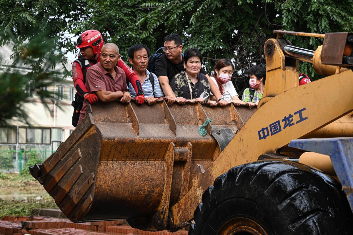 Residents ride on a front loader to cross a flooded street after heavy rains at Taishitun village in Miyun district, on the outskirts of Beijing on July 28, 2025. Photo by Jade GAO / AFP