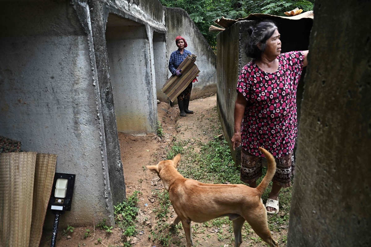 Wanta Putmo (C) and Poon Tongtuedee (R), farmers who refused to evacuate the red zone near the Thai-Cambodian border, sort out floor mats at a bunker on the grounds of a temple in the Thai border province of Surin on July 29, 2025. (Photo by Lillian SUWANRUMPHA / AFP)
