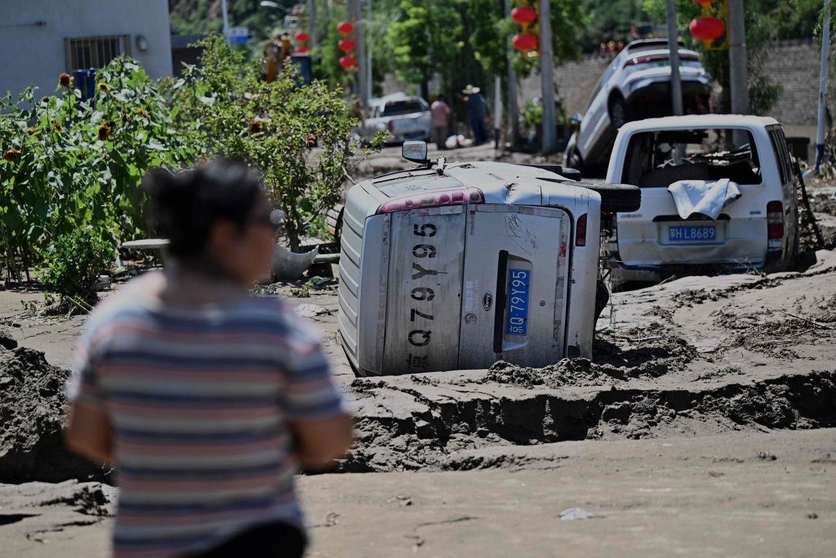 A man looks at flood damaged cars seen following heavy rains over the past few days in Huairou district, on the outskirts of Beijing on July 30, 2025. Photo by Pedro Pardo / AFP