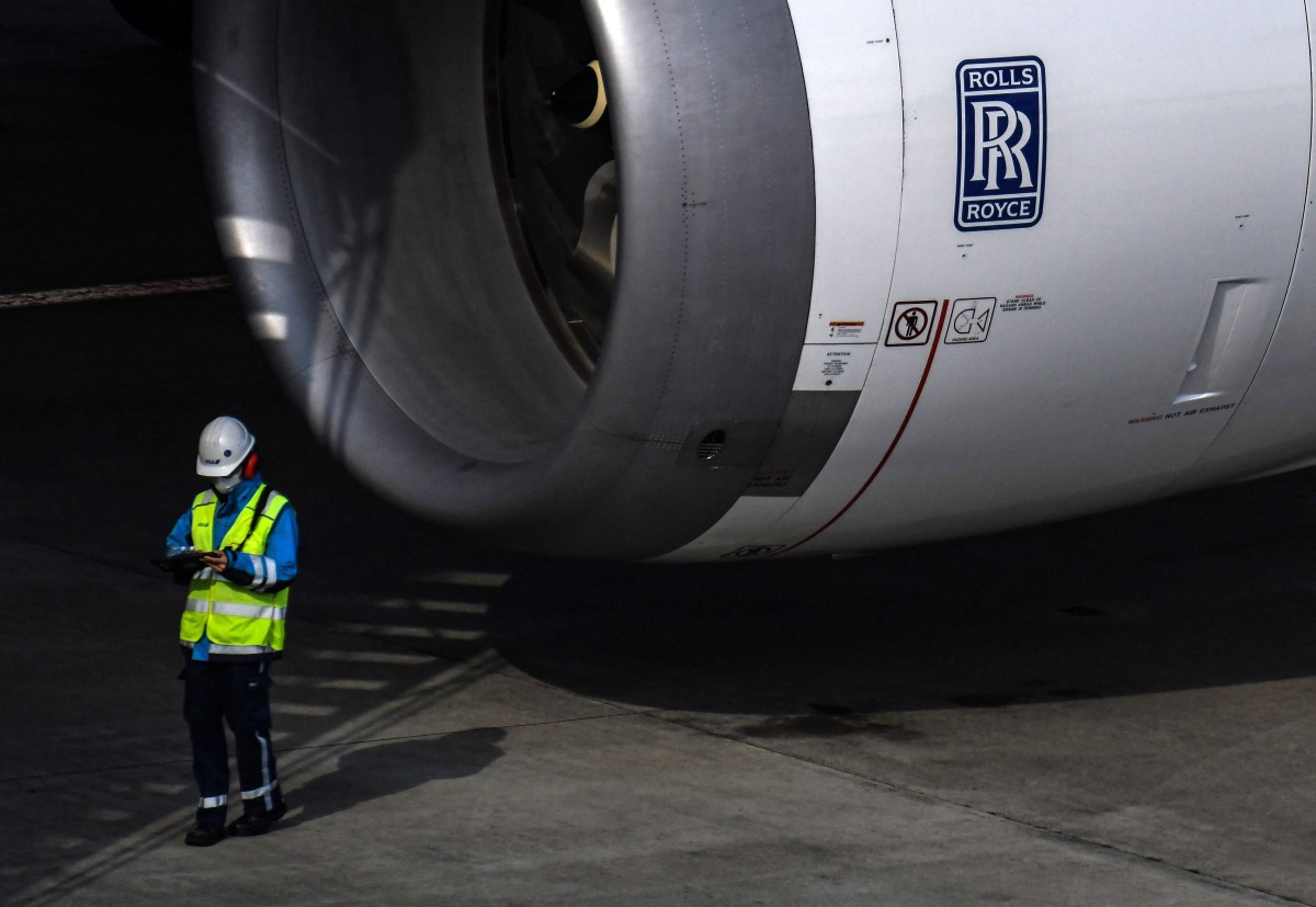 Workers stand next to a Rolls Royce aircraft engine on a passenger plane at Tokyo's Haneda airport on January 29, 2021. Photo by CHARLY TRIBALLEAU / AFP