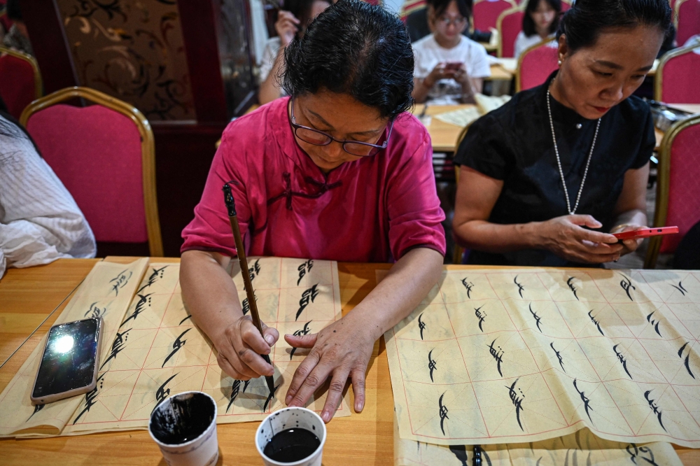 The photo taken on July 23, 2025 shows people learning Nushu calligraphy in a hotel conference room repurposed as a temporary classroom in Jiangyong county, southern China's Hunan province.(Photo by Jade Gao / AFP) 