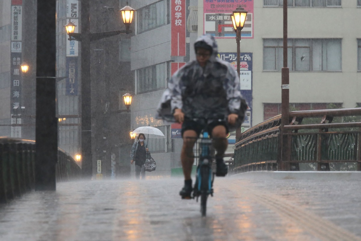 People cycle and walk in heavy rain in the city of Kumamoto, Kumomoto prefecture, southwestern Japan, on August 11, 2025. Photo by JIJI Press / AFP