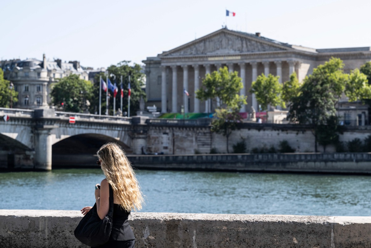 A woman walks past the Seine River and the French National Assembly, the lower House of Parliament, in Paris on August 11, 2025, amid a heatwave in Europe. (Photo by Martin LELIEVRE / AFP)