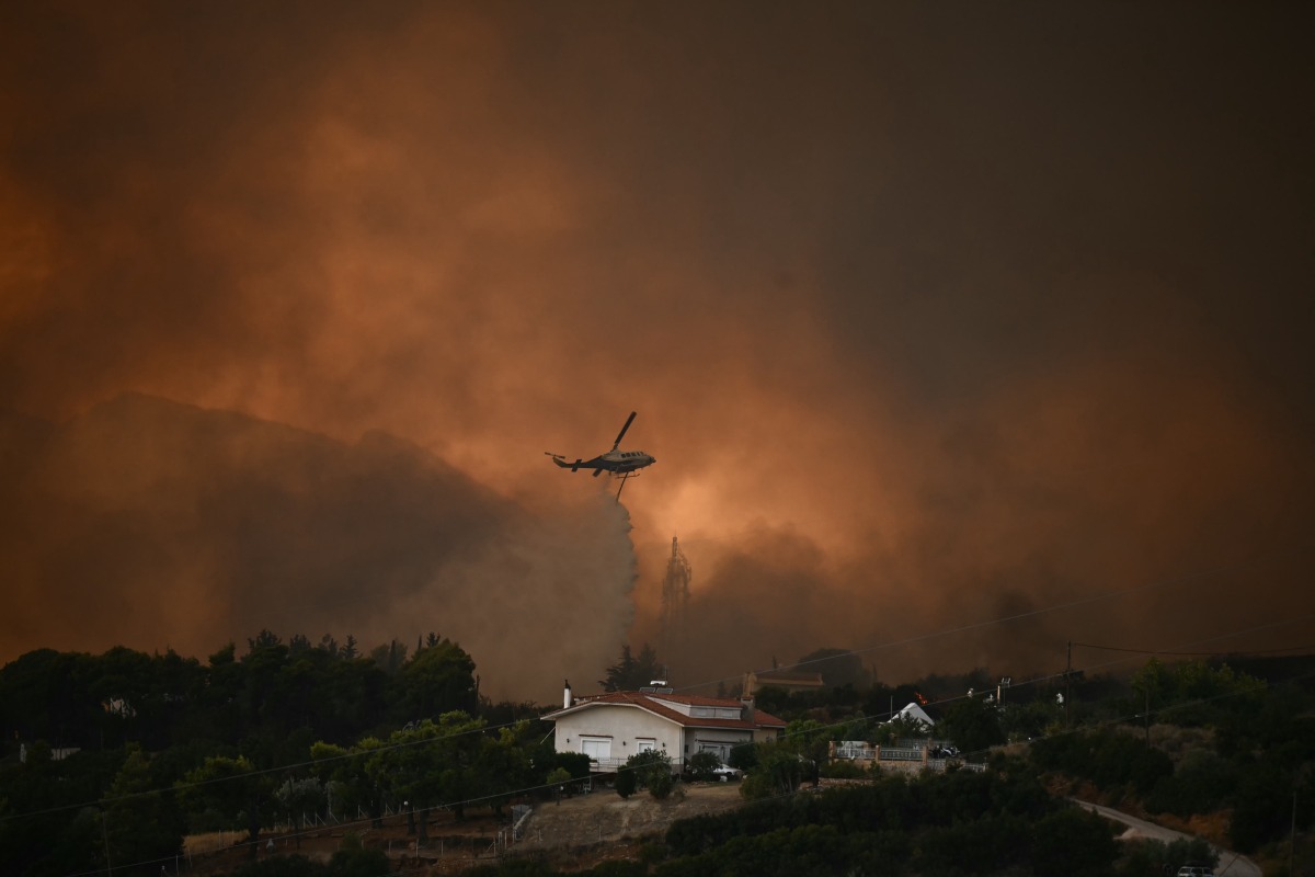 A firefighting helicopter drops water over a wildfire near the city of Patras, western Greece on August 13, 2025. Greece on August 13, 2025 battled to contain more than 20 wildfires including one menacing its third-largest city Patras as a heatwave stoked blazes and forced the evacuation of thousands in southern Europe. (Photo by Aris MESSINIS / AFP)