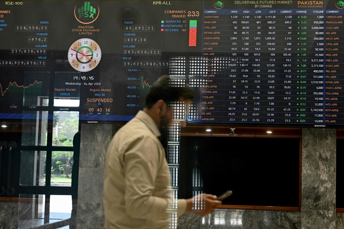 A stockbroker walks past share prices on a financial market board during a trading session at the Pakistan Stock Exchange (PSX) in Karachi on April 9, 2025. (Photo by Rizwan TABASSUM / AFP)