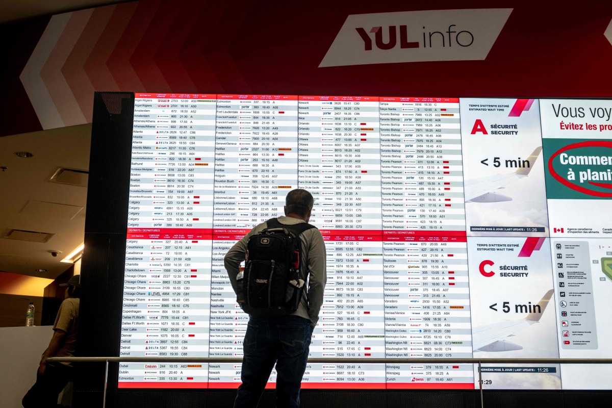 A person looks at a flight board with many cancellations for Air Canada flights at Pierre-Elliott Trudeau Airport in Montreal, Quebec, Canada, on August 17, 2025. (Photo by ANDREJ IVANOV / AFP)