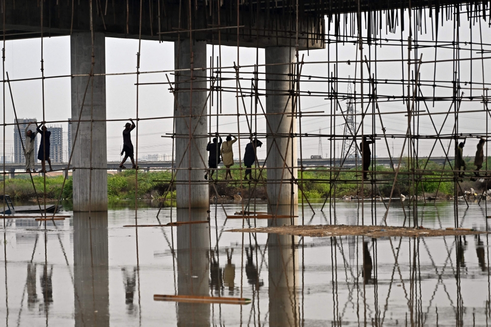 Labourers work at a flooded construction site after heavy monsson rains in Karachi on August 20, 2025. (Photo by Rizwan Tabassum / AFP)