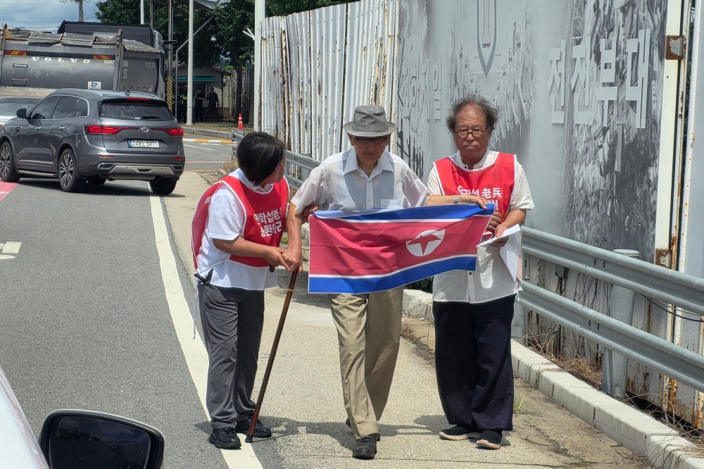 Ahn Hak-sop (C), a former North Korean soldier, holds a North Korean flag near a military checkpoint on the Tongil bridge in the border city of Paju on August 20, 2025. (Photo by YONHAP / AFP) 