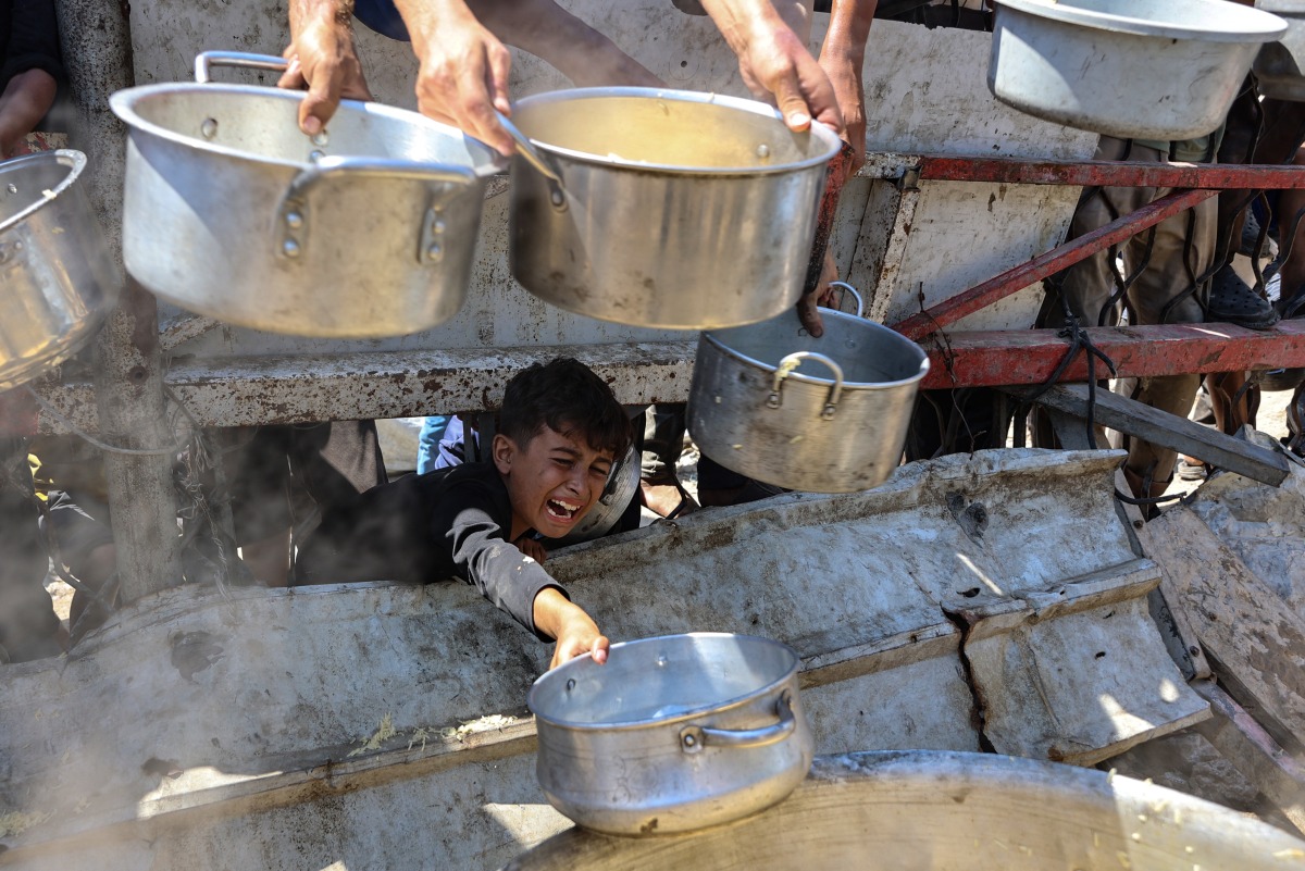 A Palestinian boy extends an empty pot in front of a charity kitchen to receive cooked rice, in Gaza City on August 23, 2025. Photo by Omar AL-QATTAA / AFP.
